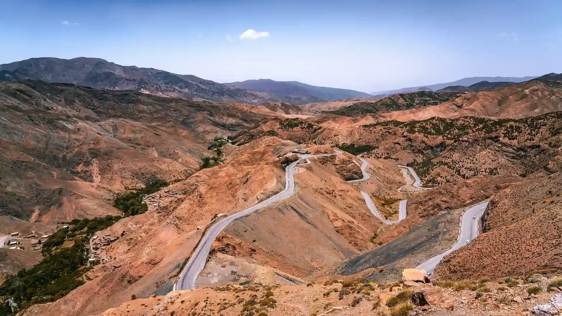 Camino sinuoso a través de montañas secas y marrones bajo un cielo azul.