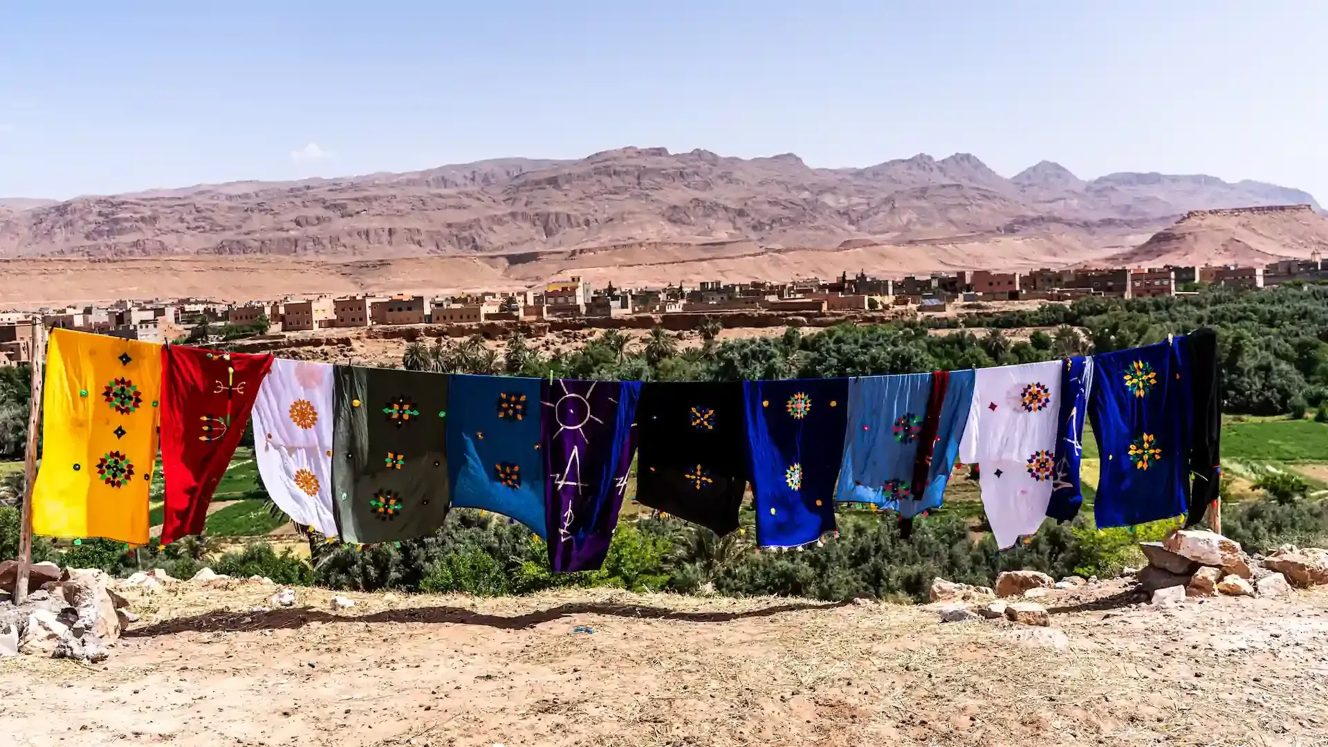 Telas de colores secándose en un tendedero en un pueblo del desierto con montañas al fondo.