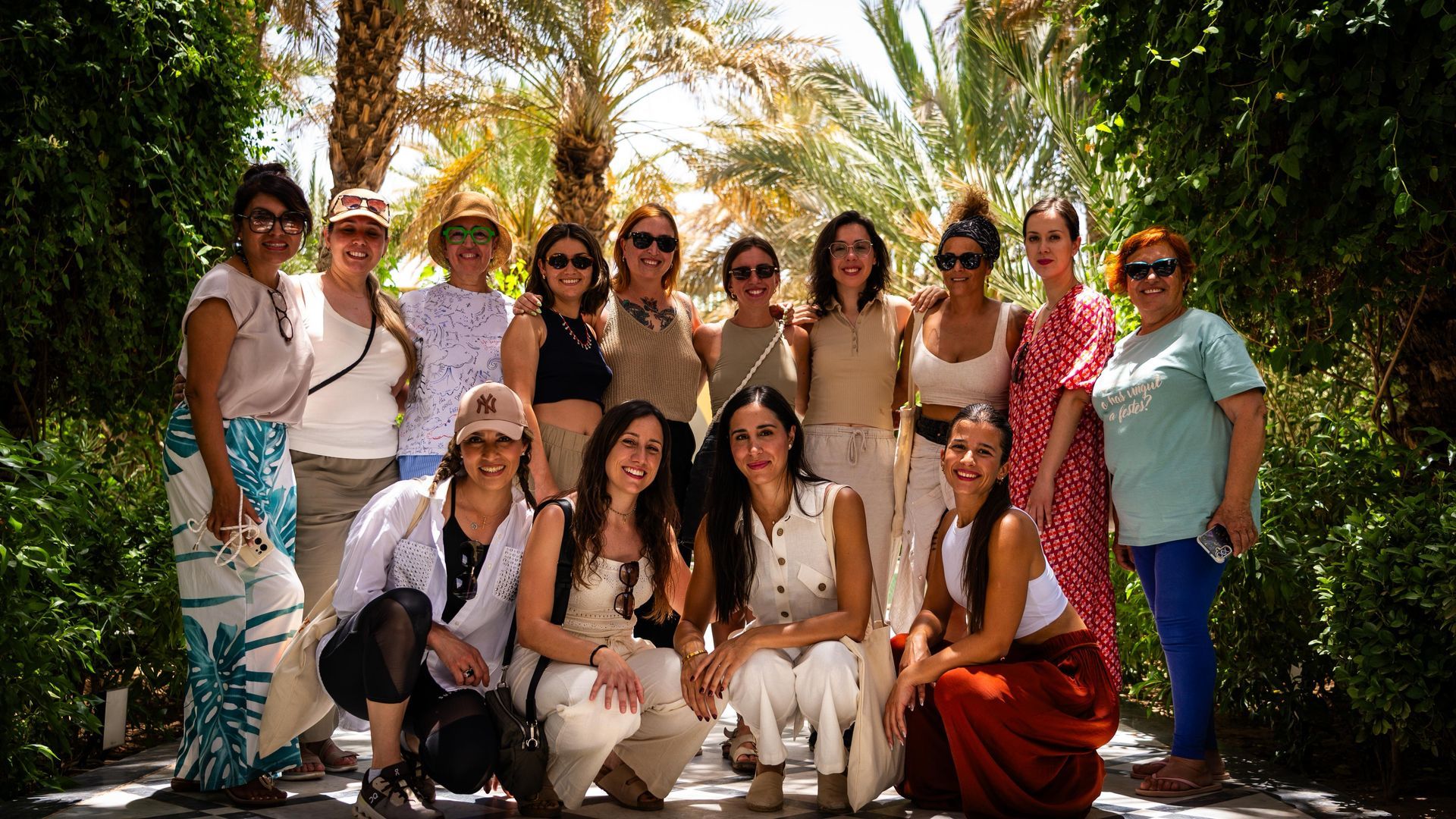 Un grupo de catorce mujeres posando para una foto a lo largo de un sendero frondoso y arbolado en un día soleado.