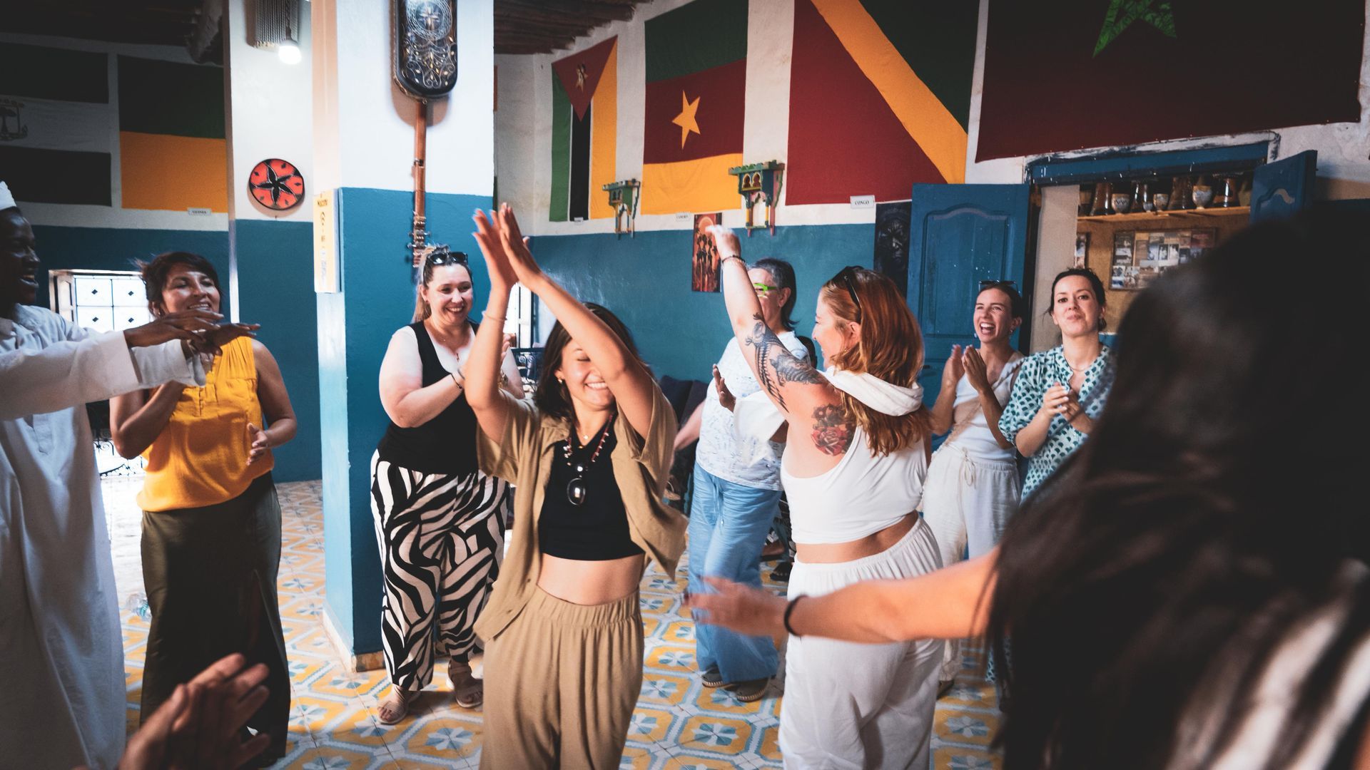 Un grupo diverso de personas baila en una colorida sala decorada con banderas, sonriendo y aplaudiendo en un ambiente alegre.