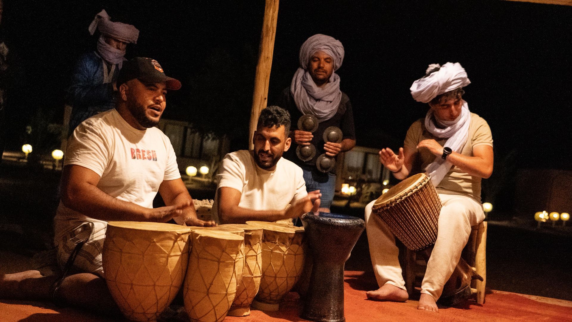 Cuatro personas tocan tambores tradicionales en un entorno exterior con poca luz por la noche.